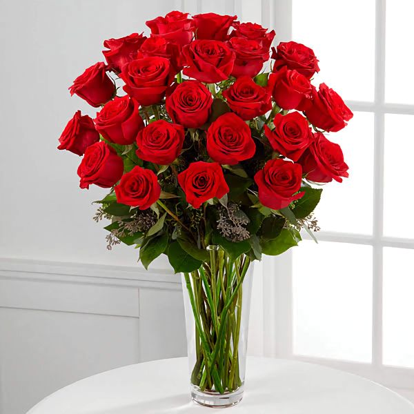 a vase filled with red roses sitting on top of a white table next to a window