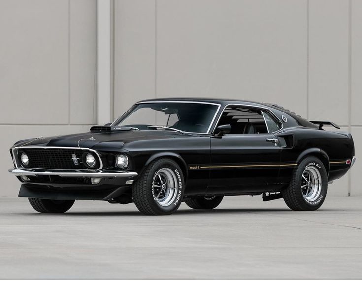 an old black muscle car parked in front of a building