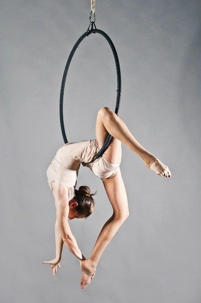 a woman is doing aerial acrobatics in the air with a hoop above her head