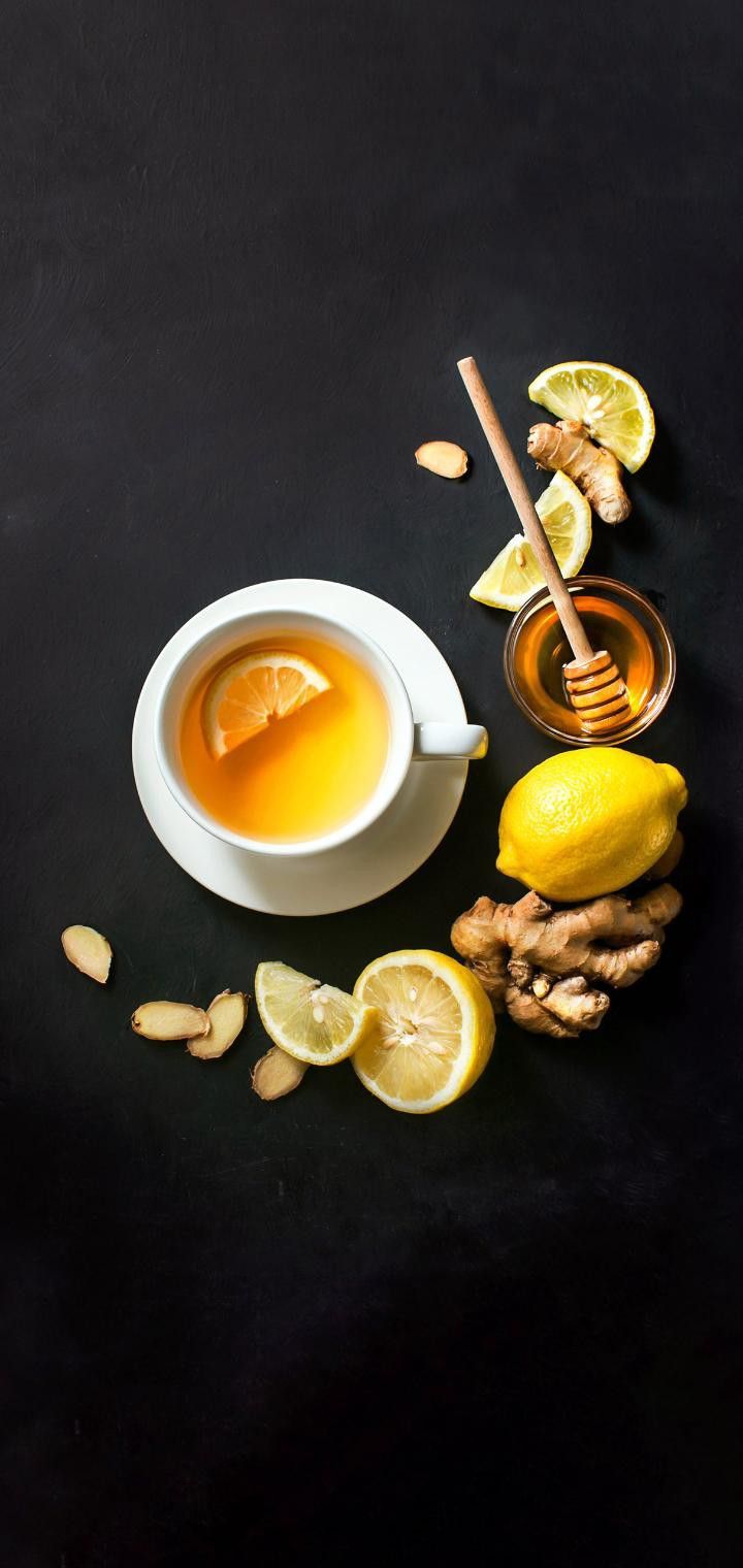 a cup of tea with lemons, nuts and honey on a black table top