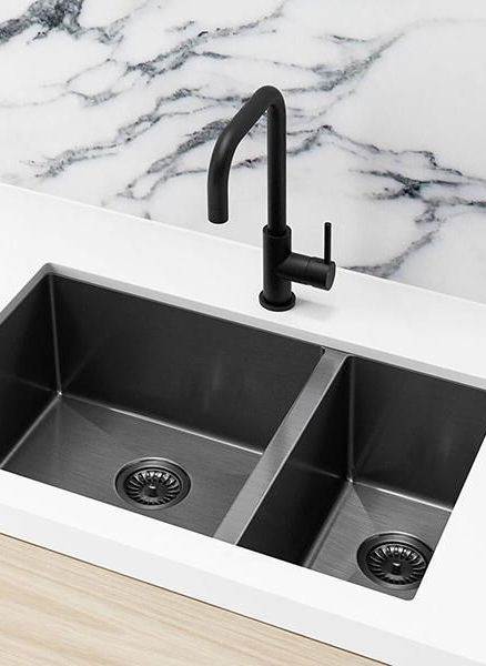 a kitchen sink with two black faucets and marble counter top in the background