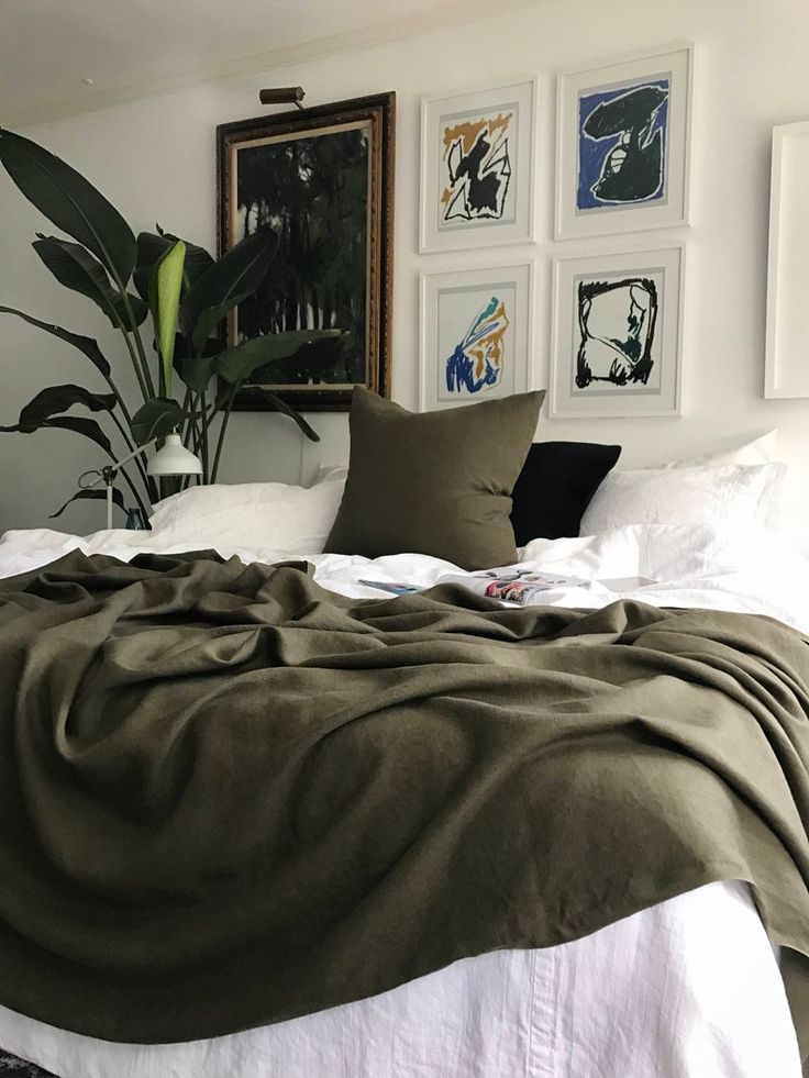 an unmade bed in a white room with pictures on the wall and green plants