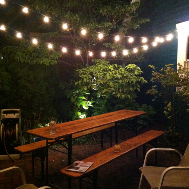 an outdoor table and benches are lit up by string lights in the garden at night