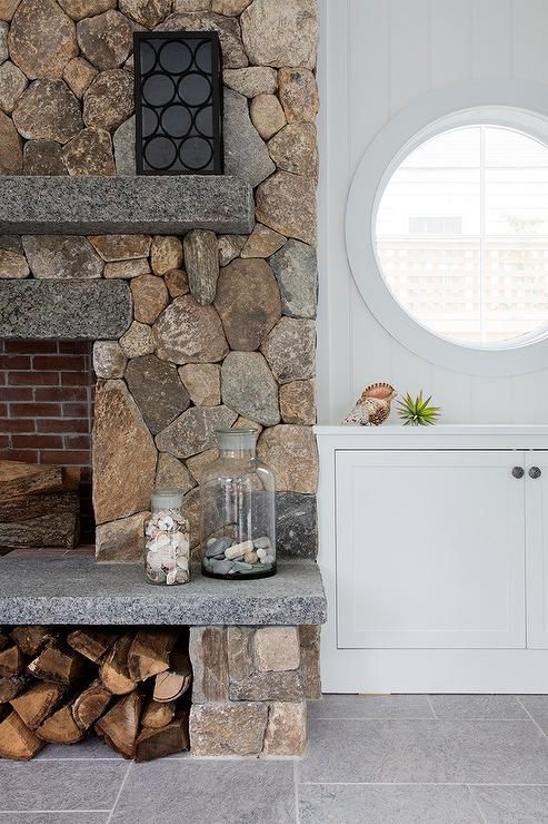 a stone fireplace in a living room next to a window with a round window on the wall