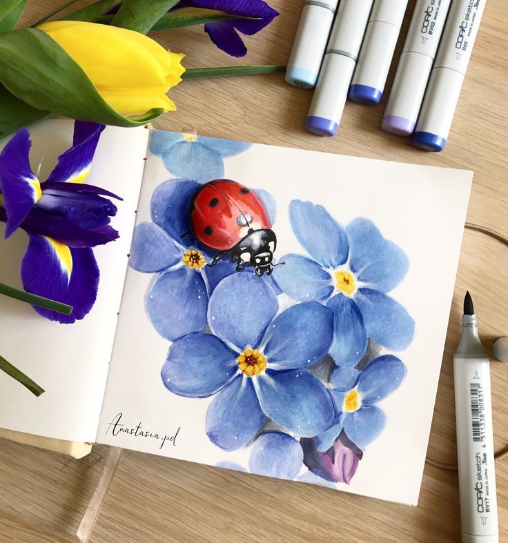 a lady bug sitting on top of a blue flower next to crayons and markers