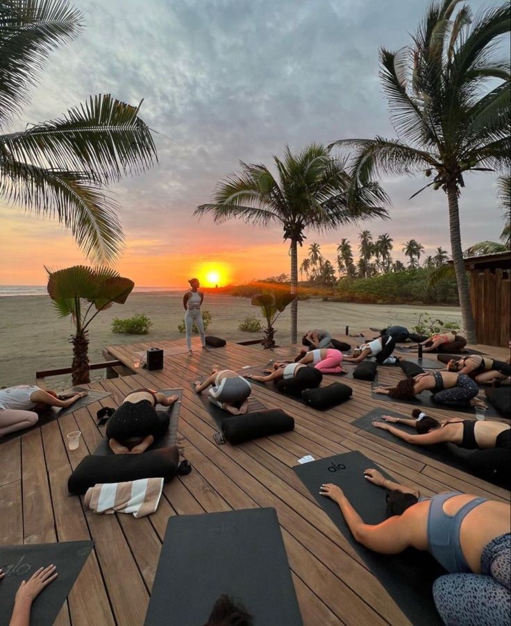 a group of people doing yoga on a wooden deck near the ocean with palm trees