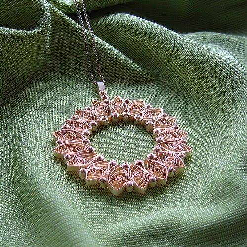 a pink necklace is sitting on a green cloth and has an intricate design in the middle