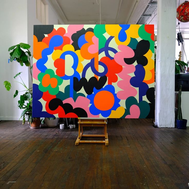 a large colorful painting sitting on top of a hard wood floor next to a potted plant