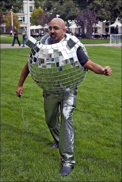 a man is walking in the grass with a giant mirror ball on his back and arms