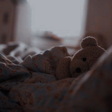 a brown teddy bear laying on top of a bed covered in blankets and blanketspread