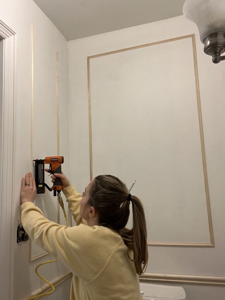 a woman is using a drill to fix a hole in the wall