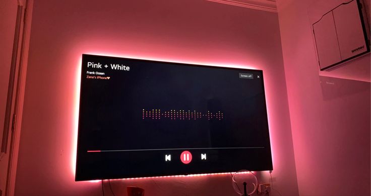 a flat screen tv mounted to the side of a wall with pink lights on it