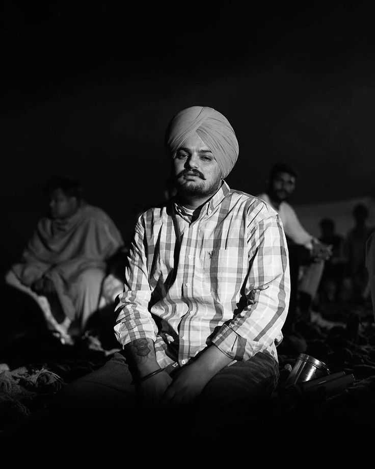 a man sitting on the ground in front of other men and one is wearing a turban