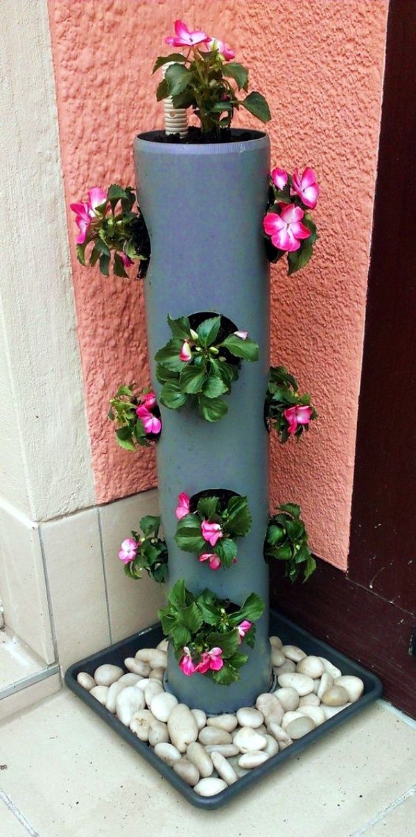 a tall planter with pink flowers and green leaves on it sitting in front of a building