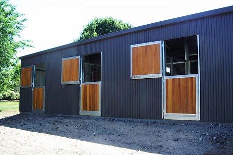 the side of a metal building with windows and wood shutters on both sides, in front of some trees