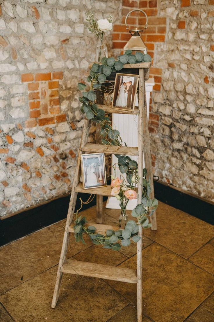 a wooden ladder decorated with greenery and photos on it in front of a brick wall