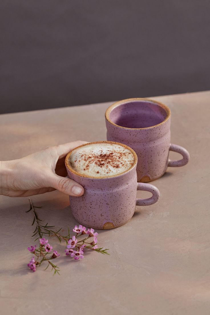 two purple coffee cups sitting on top of a table next to each other with one cup filled with liquid