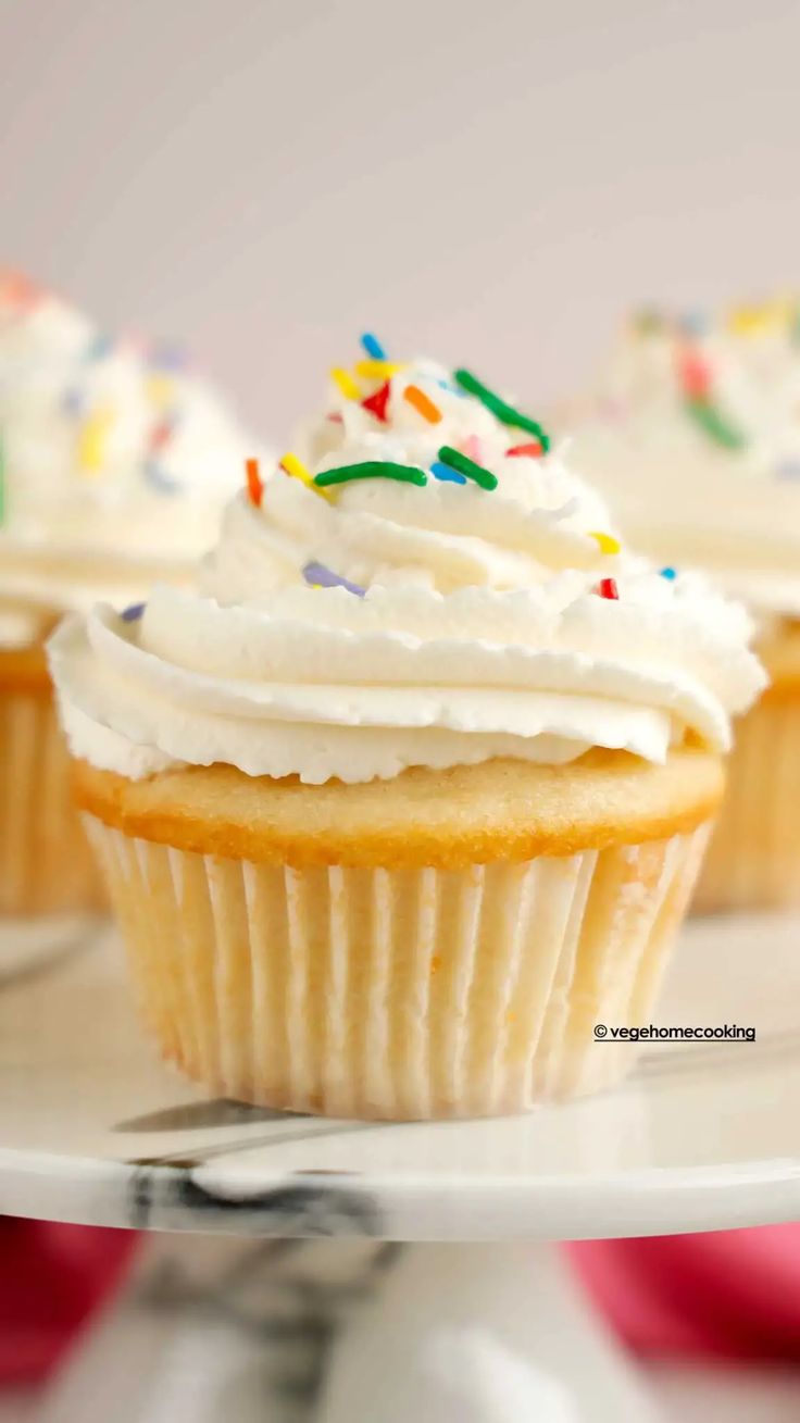 three cupcakes with white frosting and sprinkles on a plate