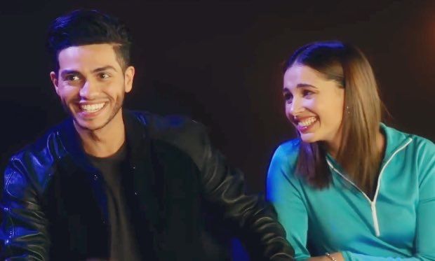 a man and woman sitting next to each other in front of a black background smiling