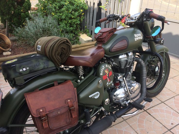 a green motorcycle parked next to a fence with a bag on it's back