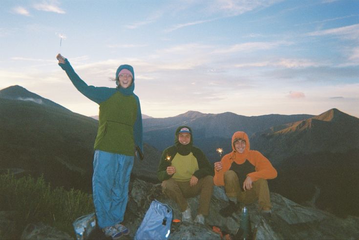 three people sitting on top of a mountain holding sparklers