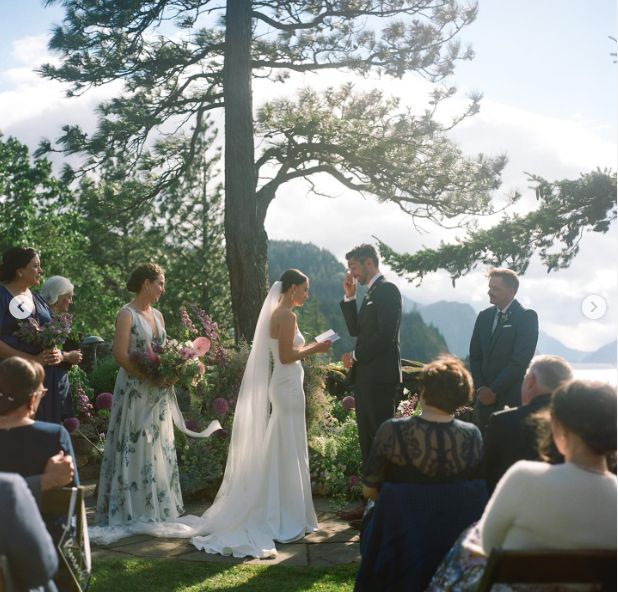 a bride and groom standing at the end of their wedding ceremony under a pine tree