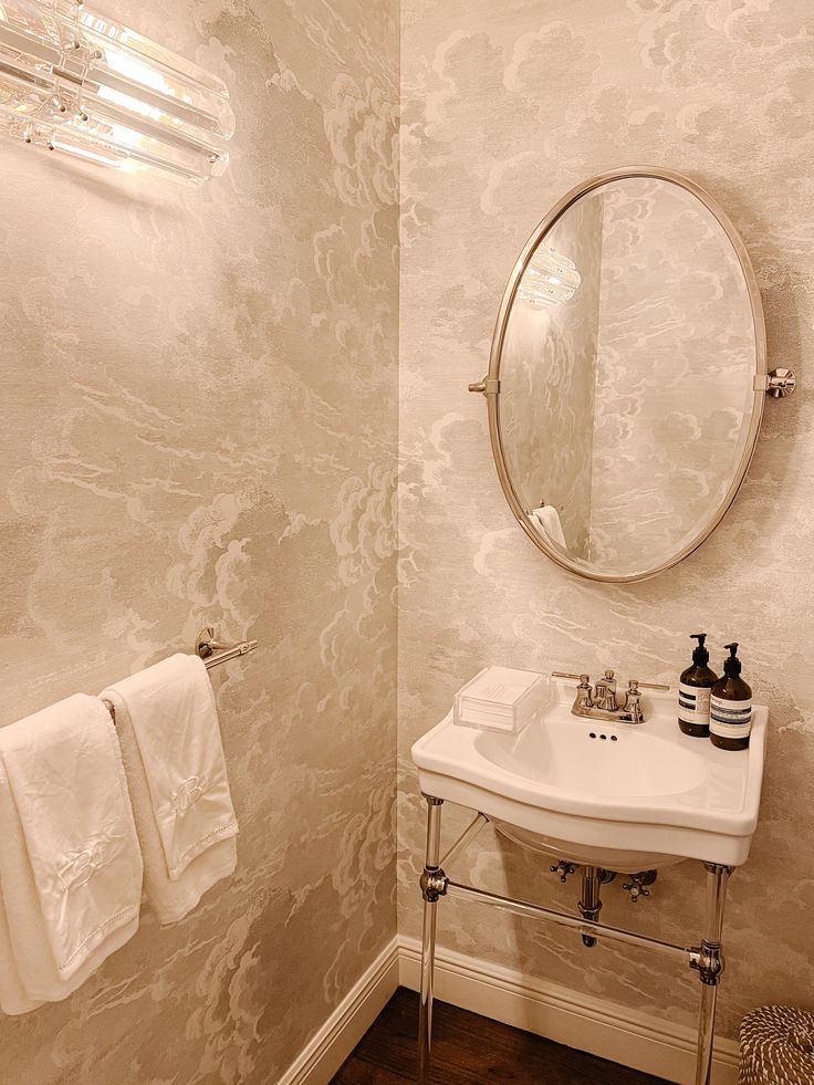 a white sink sitting under a round mirror in a bathroom next to a towel rack