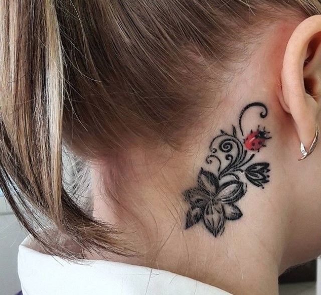 a woman's neck with a flower tattoo on her left side behind the ear