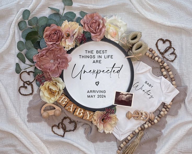 a baby announcement with flowers and other items on a white cloth covered bed sheet that says, the best things in life are unexpected