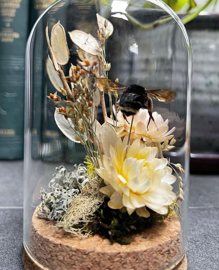 a glass clochel with flowers and a bee in it on top of a table