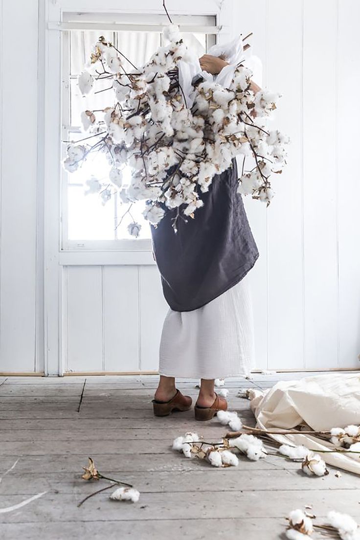 a woman standing in front of a window holding a large bouquet of cotton flowers on her shoulder