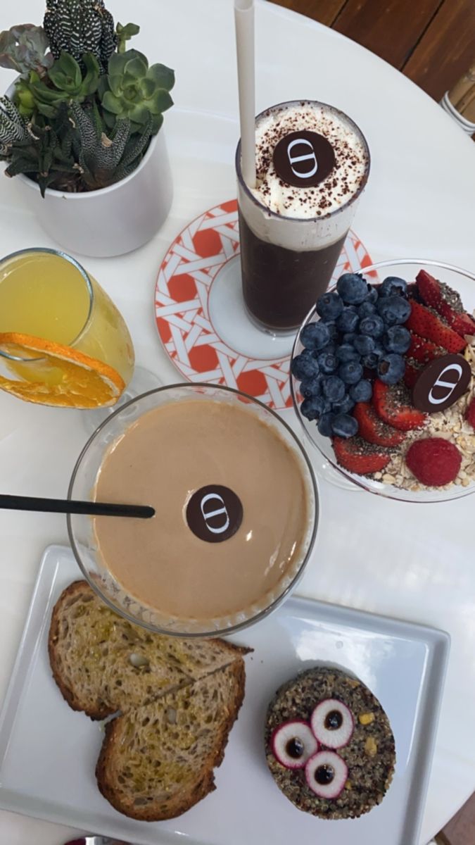 an assortment of breakfast foods on a white table with two cups of coffee and fruit