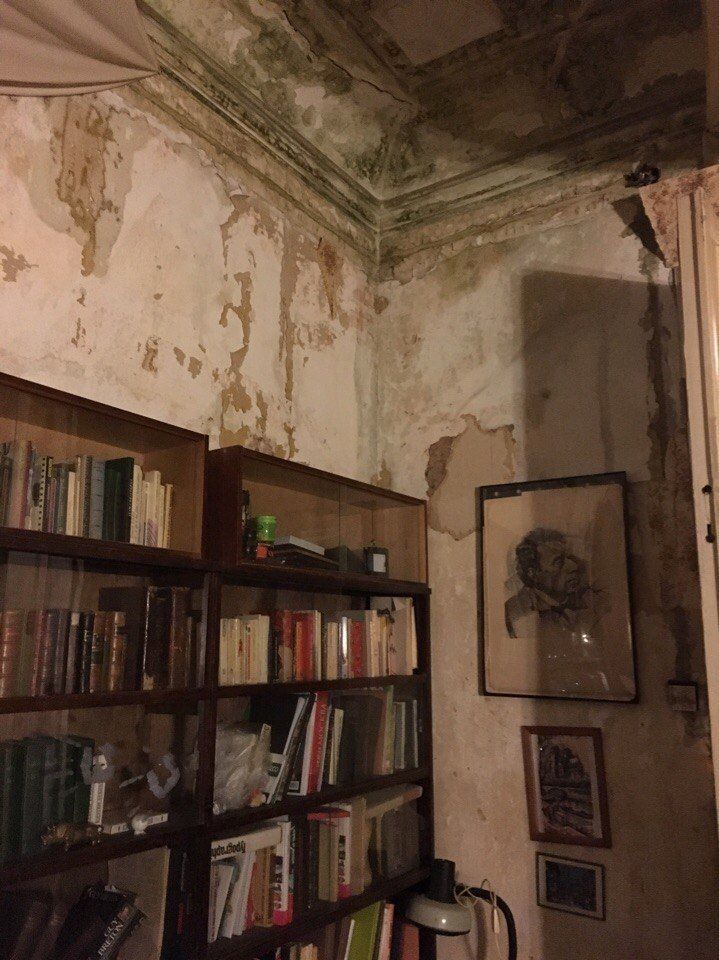 a bookshelf filled with lots of books next to a wall covered in peeling paint