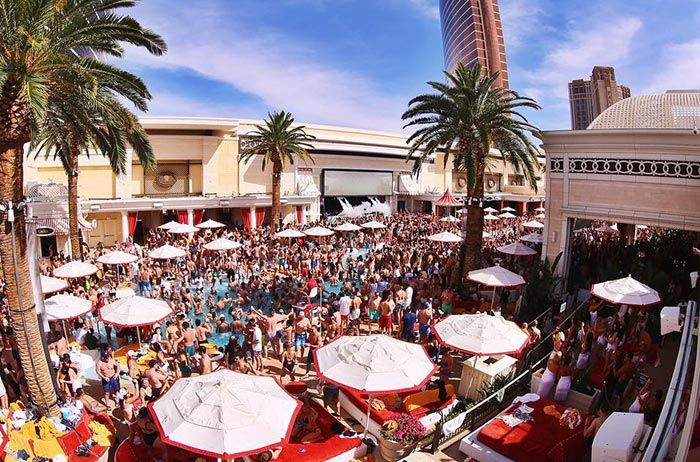 a crowd of people standing around tables with umbrellas on them in front of buildings