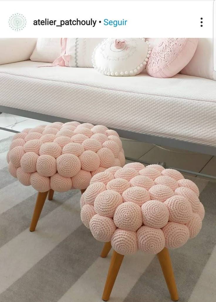 two pink poufles sitting on wooden legs in front of a white couch with pillows