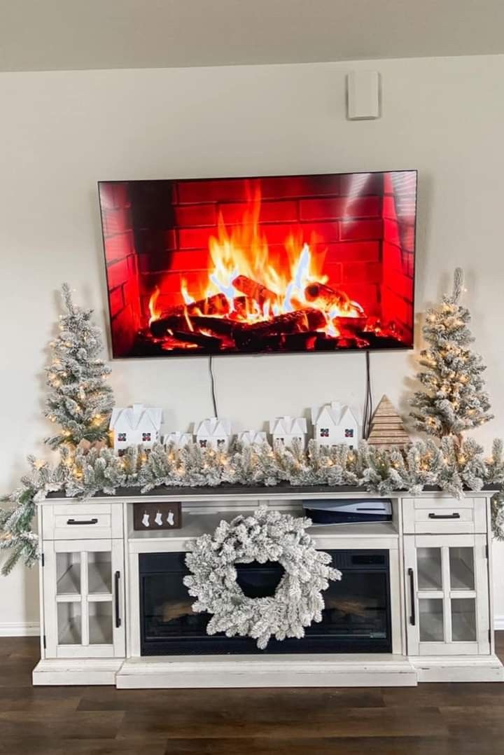 a living room with christmas decorations and a large television on the wall above it's fireplace