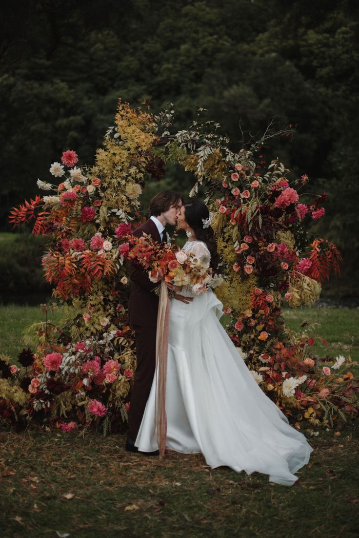 a bride and groom kissing in front of a floral arch