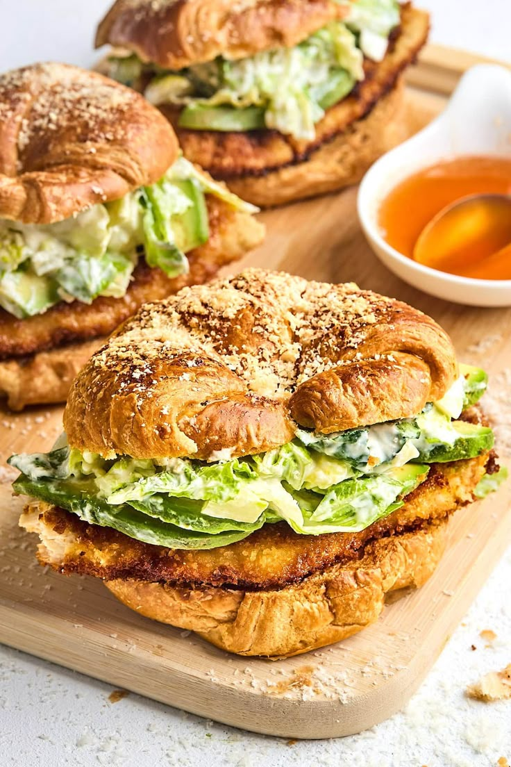 two sandwiches with lettuce and other toppings sit on a cutting board next to dipping sauce