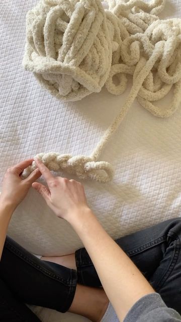 a woman laying on top of a bed next to a pile of white towels and a ball of yarn