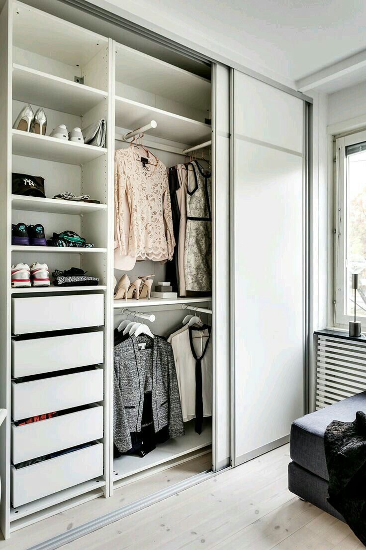 an open closet with clothes and shoes on shelves next to a window in a white room