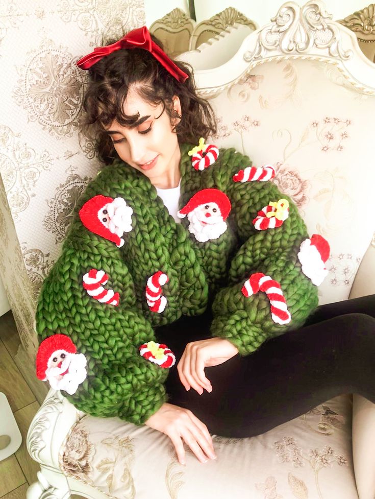 a woman sitting on top of a white couch wearing green sweaters with santa clause decorations