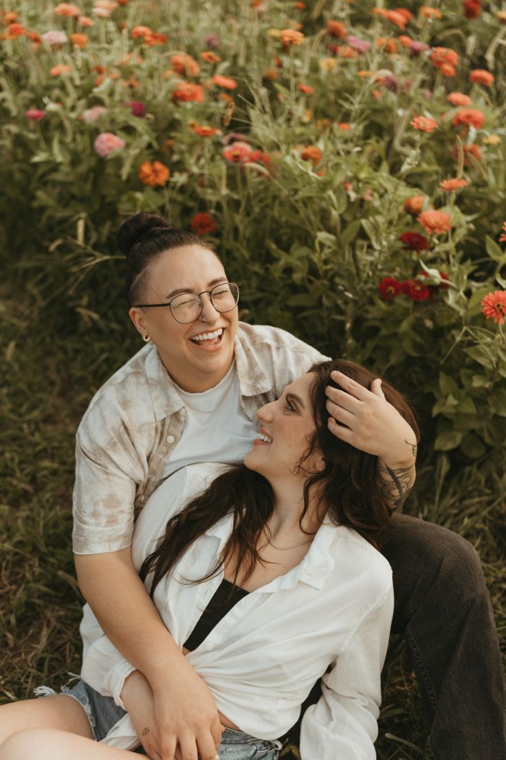 a man and woman sitting on the ground in front of flowers smiling at each other