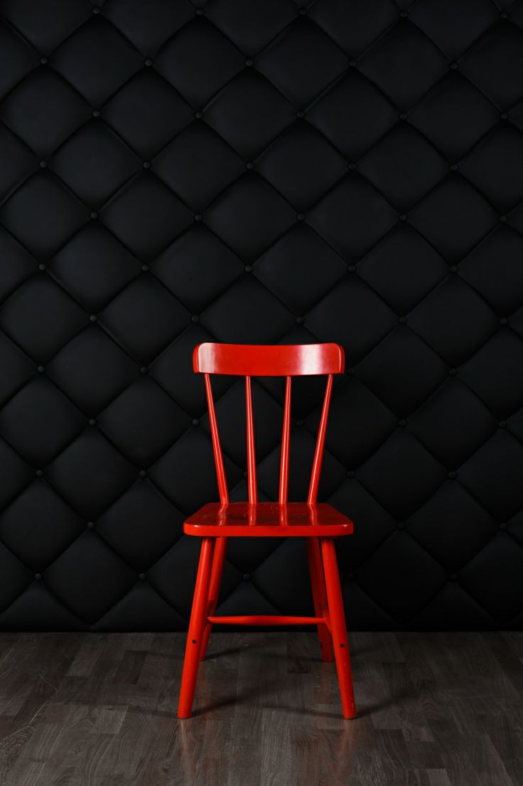 a red chair sitting on top of a hard wood floor next to a black wall