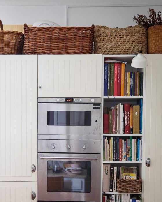 an oven and bookshelf in a kitchen with white cabinets, wicker baskets on the wall