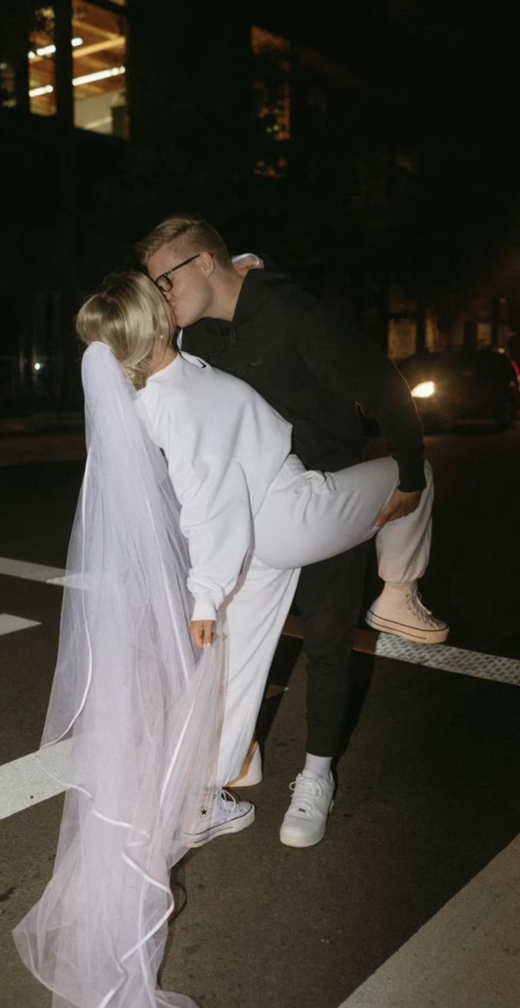 a man and woman kissing in the middle of a street at night with lights on