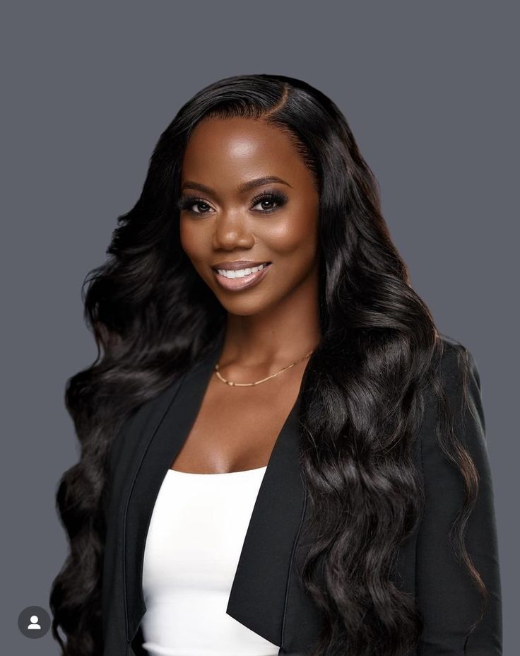 a woman with long hair wearing a black blazer and white top smiling at the camera