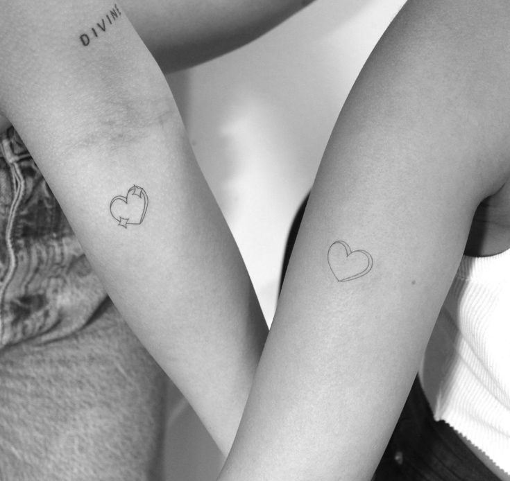 two people holding hands with tattoos on their arms, one has a heart and the other has an arrow