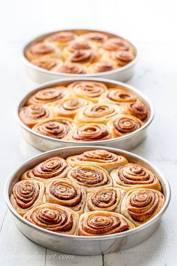 three metal pans filled with cinnamon rolls