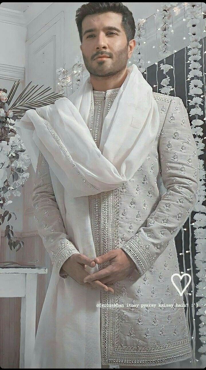 a man in a white outfit standing next to a vase with flowers and beads on it