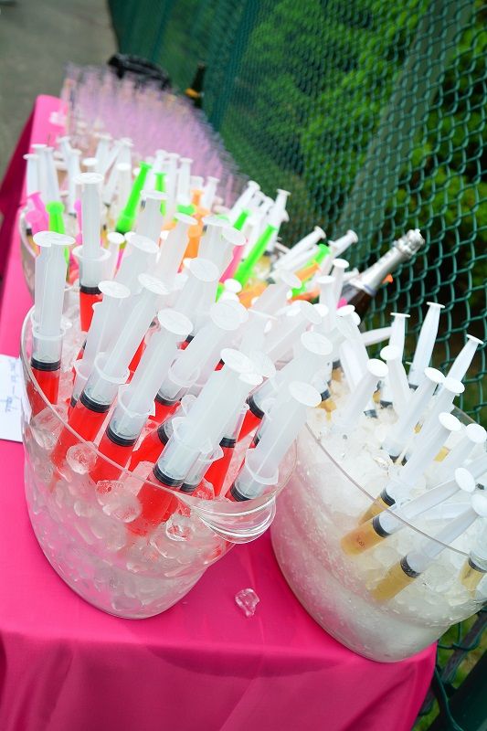 there are many different colored liquids in plastic cups on the table with pink cloths